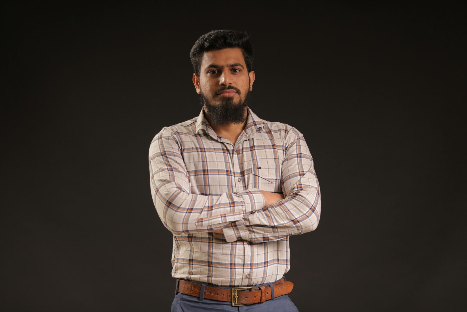 Studio portrait of a confident man with a beard and moustache, wearing a plaid shirt.